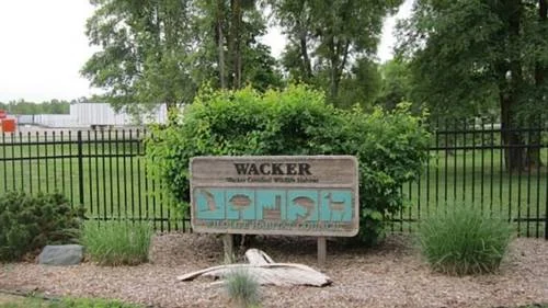 Wooden sign reading 'Wacker Certified Wildlife Habitat' with Wildlife Habitat Council logo, displayed in front of greenery and a black fence.